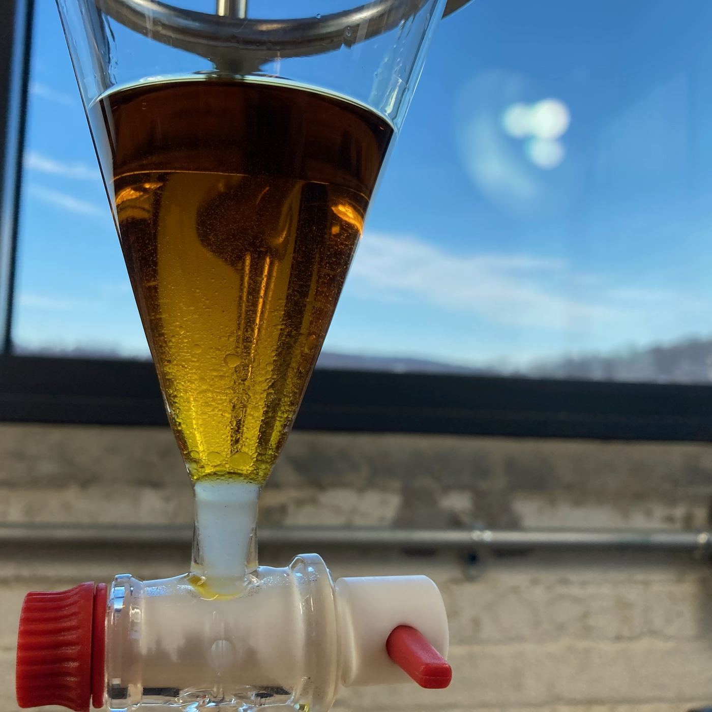 Separatory funnel holding amber CO₂ extract against a blue sky